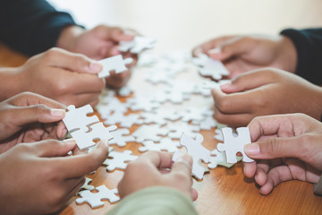 Obraz na płótnie Canvas people helping in assembling puzzle, cooperation in decision making, team support in solving problems and corporate group teamwork concept, close up view of hands connecting pieces