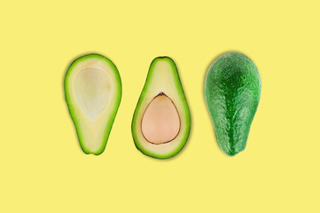 Fresh whole and halves of organic avocado with and without kernel in center of yellow table in kitchen or market. Top view. Cooking concept