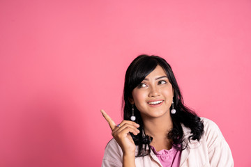 casual young woman thinking and pointing up to copyspace on pink background