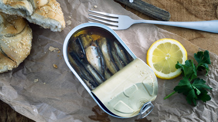 Opened fish can with lemon slice parsley and condiments on table bread with sesame seeds easy food