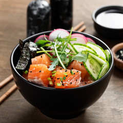Salmon fish poke bowl with rice, radish,cucumber, tomato, sesame seeds and green onion.