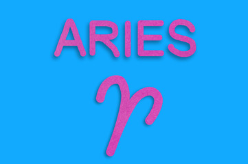 Symbol of astrological sign and word aries cut out of purple paper on blue table. Top view. Horoscope concept