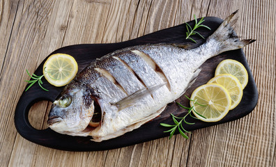 oven baked gilt-head bream on black serving board with slices lemon and rosemary