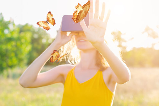 Happy beauty woman female wears summer lite yellow dress smiling and enjoy virtual reality of butterflies with vr goggles glasses outdoor in park. Active modern futuristic lifestyle leisure concept.