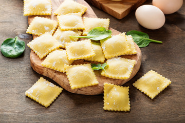 Tasty raw ravioli with flour and greens on dark background. 