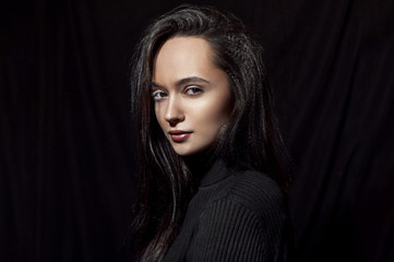 Fototapeta na wymiar Portrait of a beautiful brunette girl in a black sweater on a black background