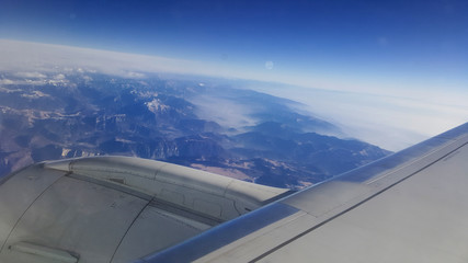Fototapeta na wymiar flying and traveling abroad, bird eye view from airplane window on the jet wing on cloudy blue sky iceberg mountain aboard morning winter time, journey backgrounds