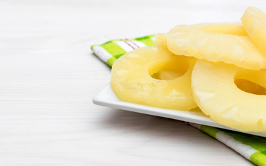 Plate with canned pineapple rings on white wooden table. Close up.