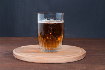 Light beer in a high glass glass on a wooden stand on brown wooden background