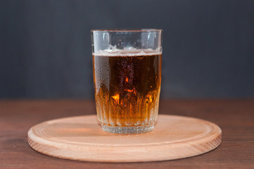Light beer in a high glass glass on a wooden stand on brown wooden background