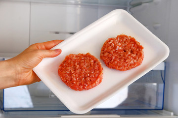 Raw Chicken Burger in container is on shelf in open fridge. Ingredient for cooking meat dishes. Uncooked meat.