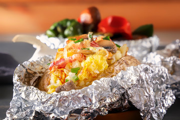 Baked potato in foil with bacon, onions and mushrooms on a gray wooden table. Close-up