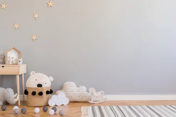 Fototapeten Stylish scandinavian newborn baby room with toys, children's chair, natural basket with teddy bear and small shelf. Modern interior with grey background walls, wooden parquet and stars pattern. © FollowTheFlow