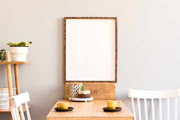 Stylish retro and sunny interior of kitchen space with wooden table with mock up photo frame, design furnitures and yellow cups. Scandinavian room decor with accessories, bamboo shelf and plants.