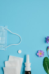 Allergy concept. Creative flat lay concept of seasonal spring and summer pollen allergy with napkins, pills, face mask, drops bottle and flowers on blue background. Top view, copy space, minimal style