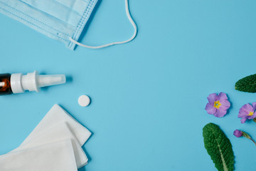 Allergy concept. Creative flat lay concept of seasonal spring and summer pollen allergy with napkins, pills, face mask, drops bottle and flowers on blue background. Top view, copy space, minimal style