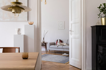Stylish scandi interior of home space with design wooden table, chairs, sofa and gold pendant lamp....