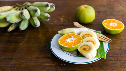 fresh fruits and sliced roll cake on a plate. banana and tangerine