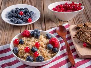 Close up view of porridge with blueberries and raspberries and grain bread on wooden background. Vegan breakfast.