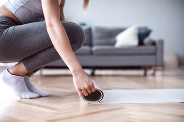 Close up woman hands unrolling mat is preparing for fitness workout in living room at home.