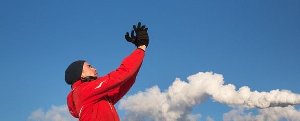 A man in red jacket looking at sky with hands holding up. Blue sky and smoke background