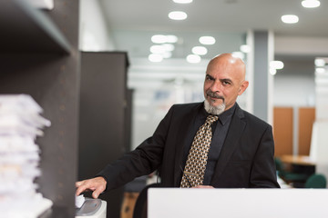 Senior bald man working in office with black suit