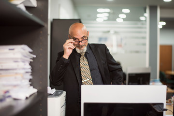 Senior bald man working in office with black suit