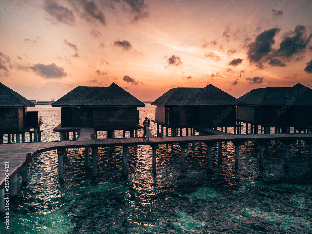 Wall mural aerial drone photo - a couple embraces during a sunrise in the maldives