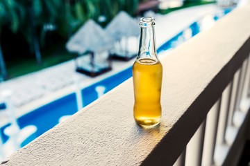 Cool refreshing bottle of lager or beer on a luxury tropical, caribbean hotel white washed balcony overlooking palm trees and resort