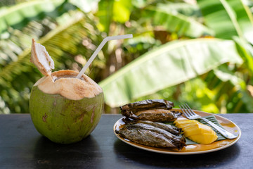 Thai style dessert, yellow mango with banana sticky rice in palm leaves and green coconut. Yellow mango and sticky rice is popular traditional dessert of Thailand.