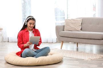 Young woman with headphones and tablet sitting on floor in living room