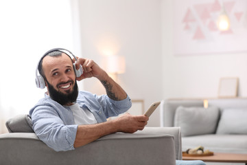 Mature man with headphones and mobile device resting in armchair at home
