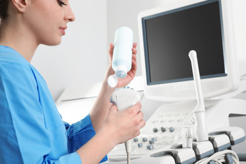 Sonographer covering ultrasound machine probe with gel in clinic, closeup