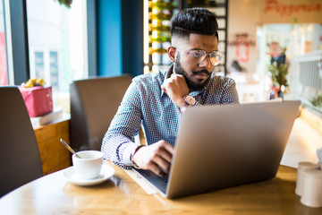 Indian man sitting at cafe against his laptop.