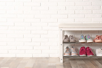 Fototapeta na wymiar Shoe storage bench with different sneakers near brick wall, space for text