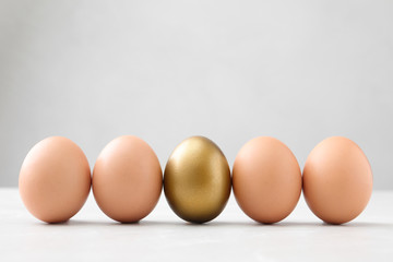 Golden egg among others on white table