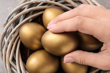 Woman taking golden egg from nest, closeup