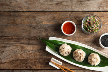 Flat lay composition with plate of tasty baozi dumplings, sesame seeds, sprouts and sauce on wooden table. Space for text