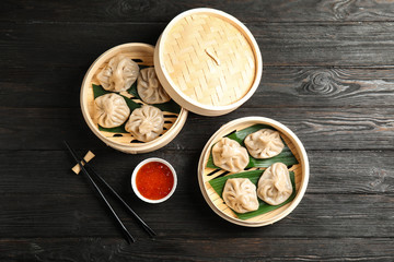 Bamboo steamers with tasty baozi dumplings, chopsticks and bowl of sauce on wooden background, top...