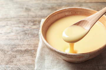 Spoon of pouring condensed milk over bowl on table, closeup with space for text. Dairy products