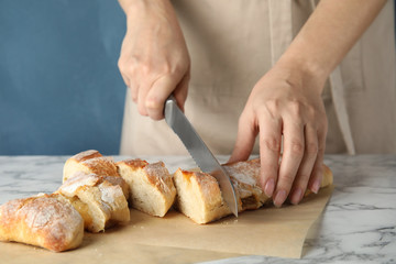 Woman cutting bread on marble table, closeup