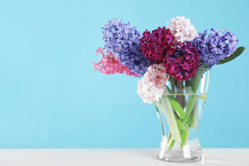 Beautiful hyacinths in glass vase on table against color background, space for text. Spring flowers