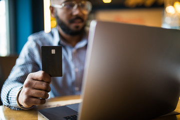 Smart young Asian man working with laptop and holding credit card for online shopping during drinking coffee in working space.