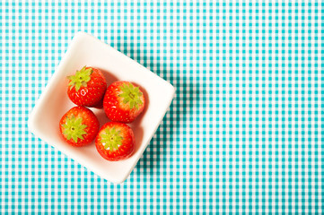 fresh strawberries in white bowl over aquamarine background with copy space