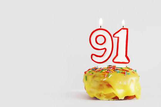 Ninety one years anniversary. Birthday cupcake with white burning candles with red border in the form of 91 number. Light gray background with copy space