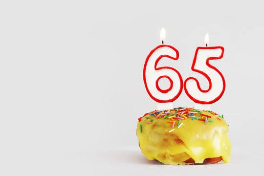 Sixty five years anniversary. Birthday cupcake with white burning candles with red border in the form of 65 number. Light gray background with copy space