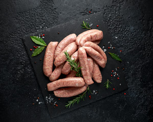Freshly made raw butchers sausages in skins with herbs on stone board