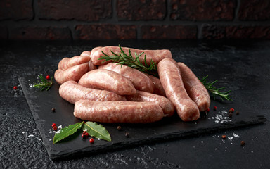 Freshly made raw butchers sausages in skins with herbs on stone board