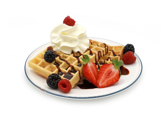 fresh belgian waffles topped with chocolate sauce, strawberries, fruits and berries  and whipped cream on a plate isolated on white background