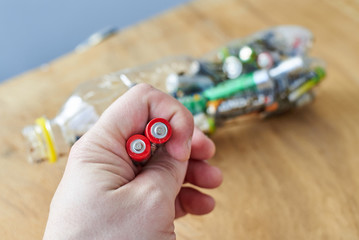 A man holds used batteries to throw in a plastic bottle, the topic of sorting garbage